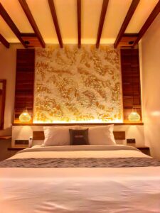 Close-up of the plush king-size bed and stunning illuminated textured gold headboard in the second-floor Deluxe Double room at Kuda Putih Pandawa Bali.