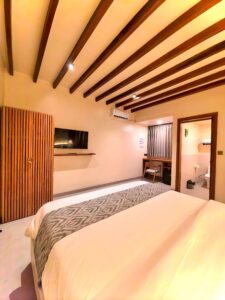 Spacious interior of the second-floor Deluxe Double room featuring a dedicated wooden desk, mini-fridge, and comfortable bedding at Kuda Putih Pandawa South Kuta.