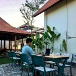 A guest working on a laptop at the outdoor garden seating area of Kuda Putih Pandawa Guesthouse, highlighting a relaxing tropical workspace for digital nomads in Bali.