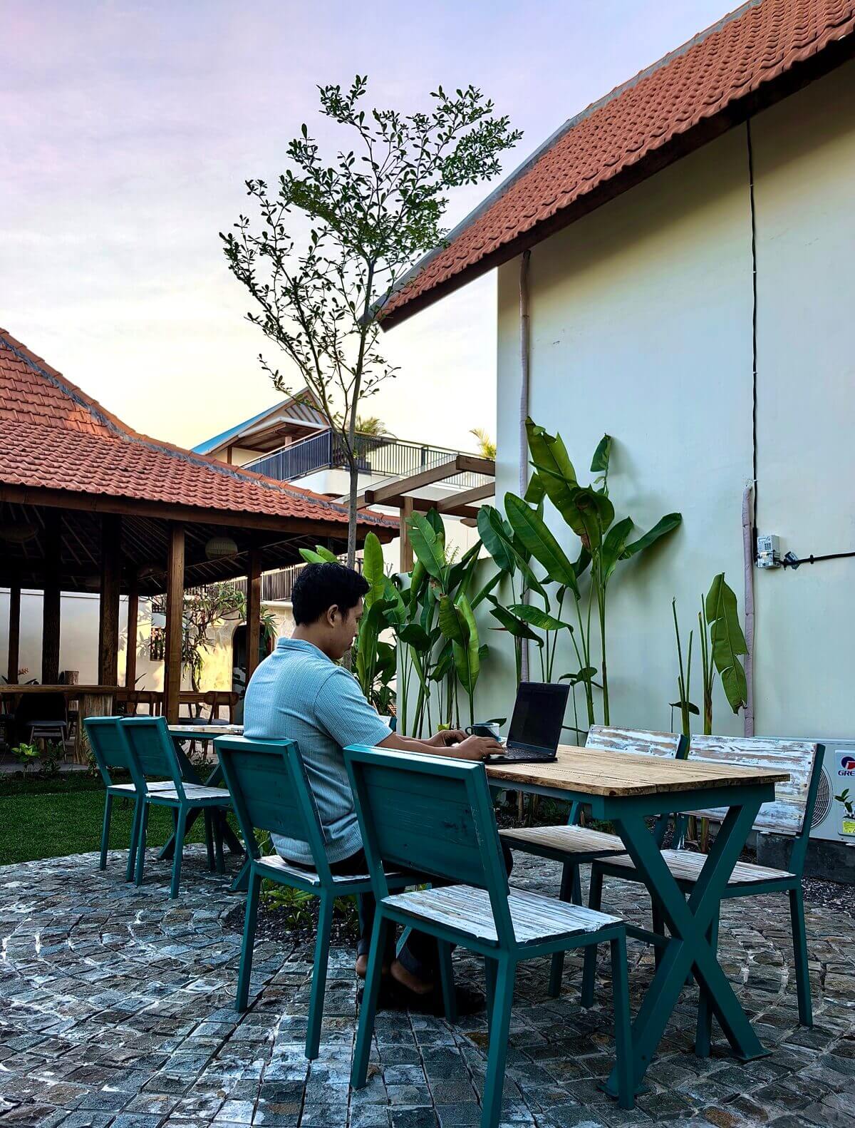 A guest working on a laptop at the outdoor garden seating area of Kuda Putih Pandawa Guesthouse, highlighting a relaxing tropical workspace for digital nomads in Bali.