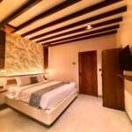 Wide interior angle highlighting the exposed wooden ceiling beams, luxurious bed, and wooden wardrobe in the Deluxe Double room at Kuda Putih Pandawa Bali.