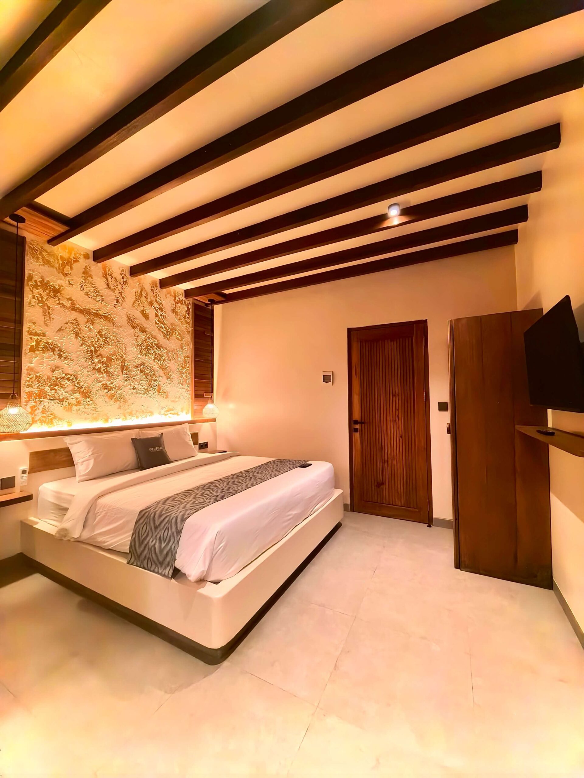 Deluxe Double (2nd Floor) Wide interior angle highlighting the exposed wooden ceiling beams, luxurious bed, and wooden wardrobe in the Deluxe Double room at Kuda Putih Pandawa Bali.