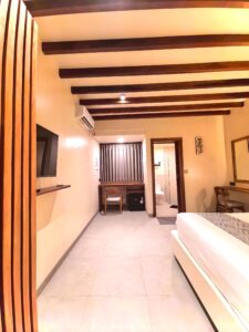 View from the entrance of the second-floor Deluxe Double room showcasing the aesthetic wooden partition, flat-screen TV, and modern layout at Kuda Putih Pandawa guesthouse.