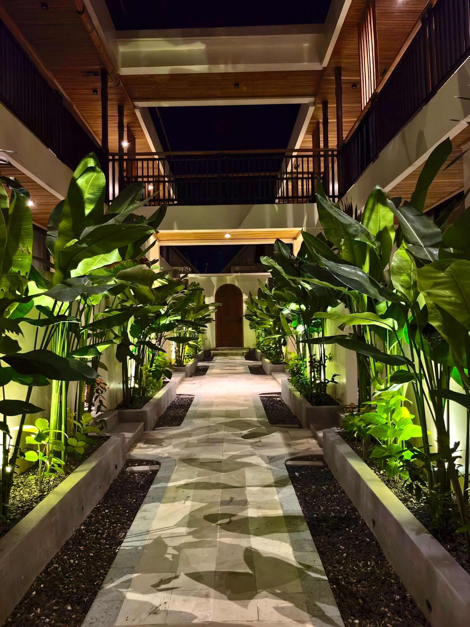 A tropical garden pathway illuminated by warm floor lights leading to a wooden door at the premium Kuda Putih Pandawa accommodation near Pandawa Beach.
