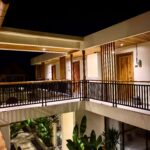 Night view of the two-story central courtyard at Kuda Putih Pandawa Guesthouse Bali, featuring tropical plants and aesthetic warm lighting.
