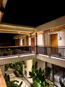 Night view of the two-story central courtyard at Kuda Putih Pandawa Guesthouse Bali, featuring tropical plants and aesthetic warm lighting.