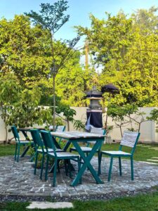 Rustic wooden table and chairs in the green tropical garden of Kuda Putih Pandawa Bali, featuring a traditional Balinese shrine in the background.