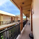 Bright daytime atmosphere along the second-floor balcony walkway at Kuda Putih Pandawa Guesthouse Bali, showcasing wooden ceilings and guest rooms.