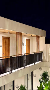 Architectural details of wooden pillars and guest room doors on the second-floor balcony of Kuda Putih Pandawa Bali with elegant night lighting.