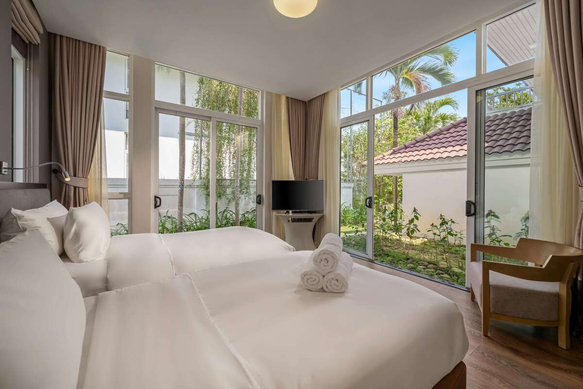 A clean, white-themed bedroom with large sliding glass doors providing direct access to a private tropical garden at Kuda Putih Pandawa.