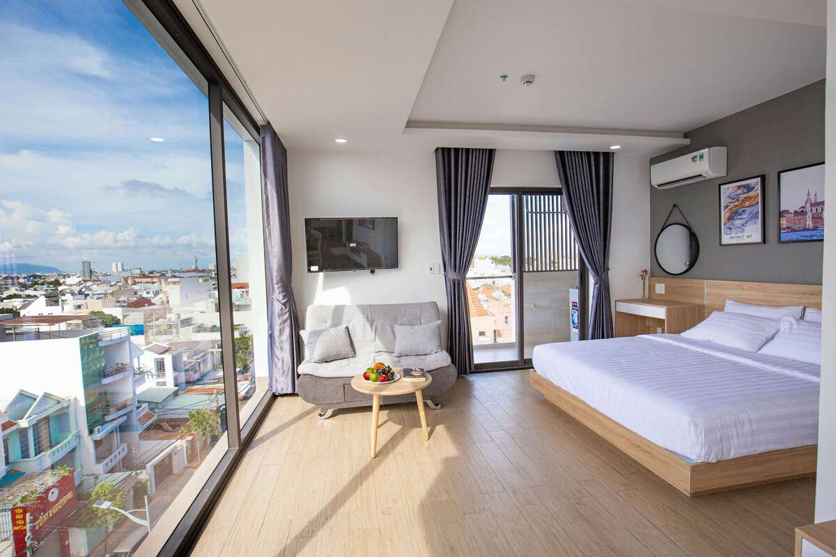 A spacious premium bedroom featuring a king-size bed, sofa, and large windows offering a city view at Kuda Putih Pandawa, Bali.