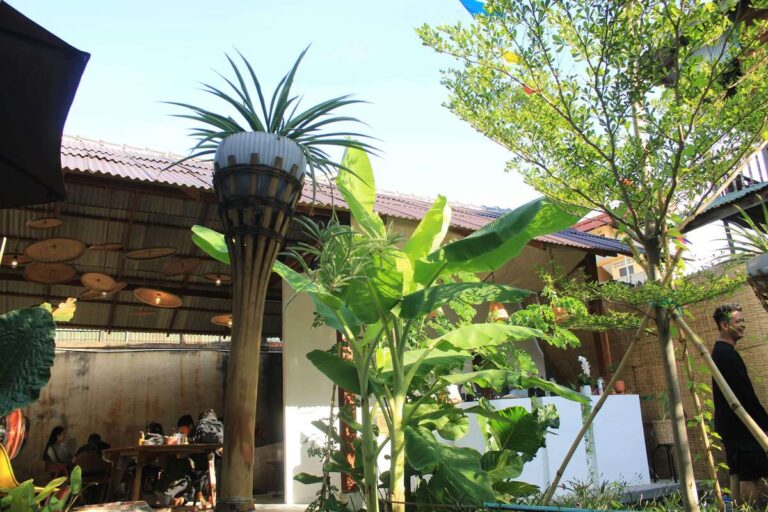 A lush semi-outdoor dining area with tropical plants and wooden chairs at Kuda Putih Pandawa Guesthouse in Bali.