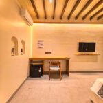 A wooden working desk, mini-refrigerator, and flat-screen TV inside the Deluxe Double room at Kuda Putih Pandawa premium accommodation near Pandawa Beach.