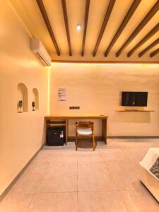 A wooden working desk, mini-refrigerator, and flat-screen TV inside the Deluxe Double room at Kuda Putih Pandawa premium accommodation near Pandawa Beach.