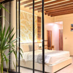 A view through glass sliding doors into the ground-floor Deluxe Double room at Kuda Putih Pandawa guesthouse in Bali, featuring a cozy bed and warm aesthetic lighting.