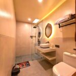 A clean, modern ensuite bathroom featuring a glass walk-in shower, floating vanity sink, and backlit mirror in the Deluxe Double room at Kuda Putih Pandawa Bali.