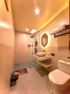 A clean, modern ensuite bathroom featuring a glass walk-in shower, floating vanity sink, and backlit mirror in the Deluxe Double room at Kuda Putih Pandawa Bali.