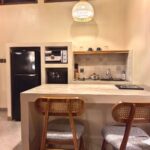 A fully equipped modern kitchenette with a dining island, rattan bar stools, and warm pendant lighting inside a premium suite at Kuda Putih Pandawa South Kuta.