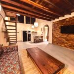 A wide view of the luxurious suite interior at Kuda Putih Pandawa Bali, showcasing a cozy living room, wooden architecture, and a modern kitchenette.