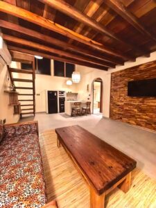 A wide view of the luxurious suite interior at Kuda Putih Pandawa Bali, showcasing a cozy living room, wooden architecture, and a modern kitchenette.
