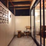A relaxing private outdoor patio at night with a wooden chair, side table, and aesthetic breeze block wall at Kuda Putih Pandawa accommodation in South Kuta.
