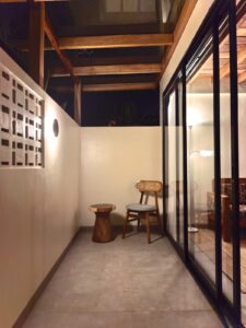 A relaxing private outdoor patio at night with a wooden chair, side table, and aesthetic breeze block wall at Kuda Putih Pandawa accommodation in South Kuta.
