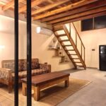 A spacious ground-floor living area featuring a wooden sofa, coffee table, and a staircase leading to the mezzanine in a premium loft at Kuda Putih Pandawa Bali.