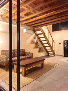 A spacious ground-floor living area featuring a wooden sofa, coffee table, and a staircase leading to the mezzanine in a premium loft at Kuda Putih Pandawa Bali.