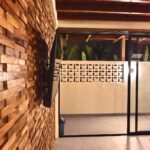 Aesthetic 3D wooden accent wall with a mounted flat-screen TV and a view of the outdoor patio at Kuda Putih Pandawa boutique guesthouse in Bali.