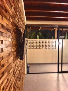 Aesthetic 3D wooden accent wall with a mounted flat-screen TV and a view of the outdoor patio at Kuda Putih Pandawa boutique guesthouse in Bali.
