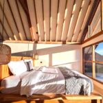 Morning sunlight illuminating a cozy king-size bed and exposed wooden ceiling architecture inside a tropical cabin at Kuda Putih Pandawa near Pandawa Beach.