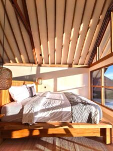 Morning sunlight illuminating a cozy king-size bed and exposed wooden ceiling architecture inside a tropical cabin at Kuda Putih Pandawa near Pandawa Beach.