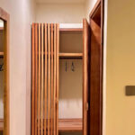 An aesthetic slatted wooden wardrobe and luggage storage space in the hallway of the Deluxe Double room at Kuda Putih Pandawa guesthouse in Bali.