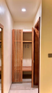 An aesthetic slatted wooden wardrobe and luggage storage space in the hallway of the Deluxe Double room at Kuda Putih Pandawa guesthouse in Bali.